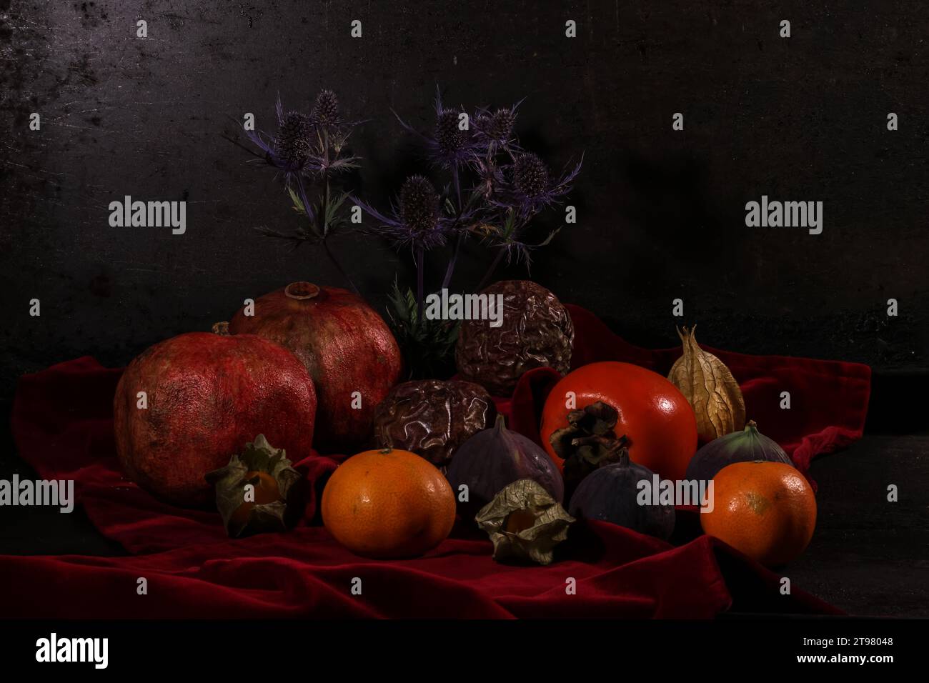 Divers fruits tropicaux et un chardon forment une nature morte sur un tissu de velours rouge foncé. Banque D'Images