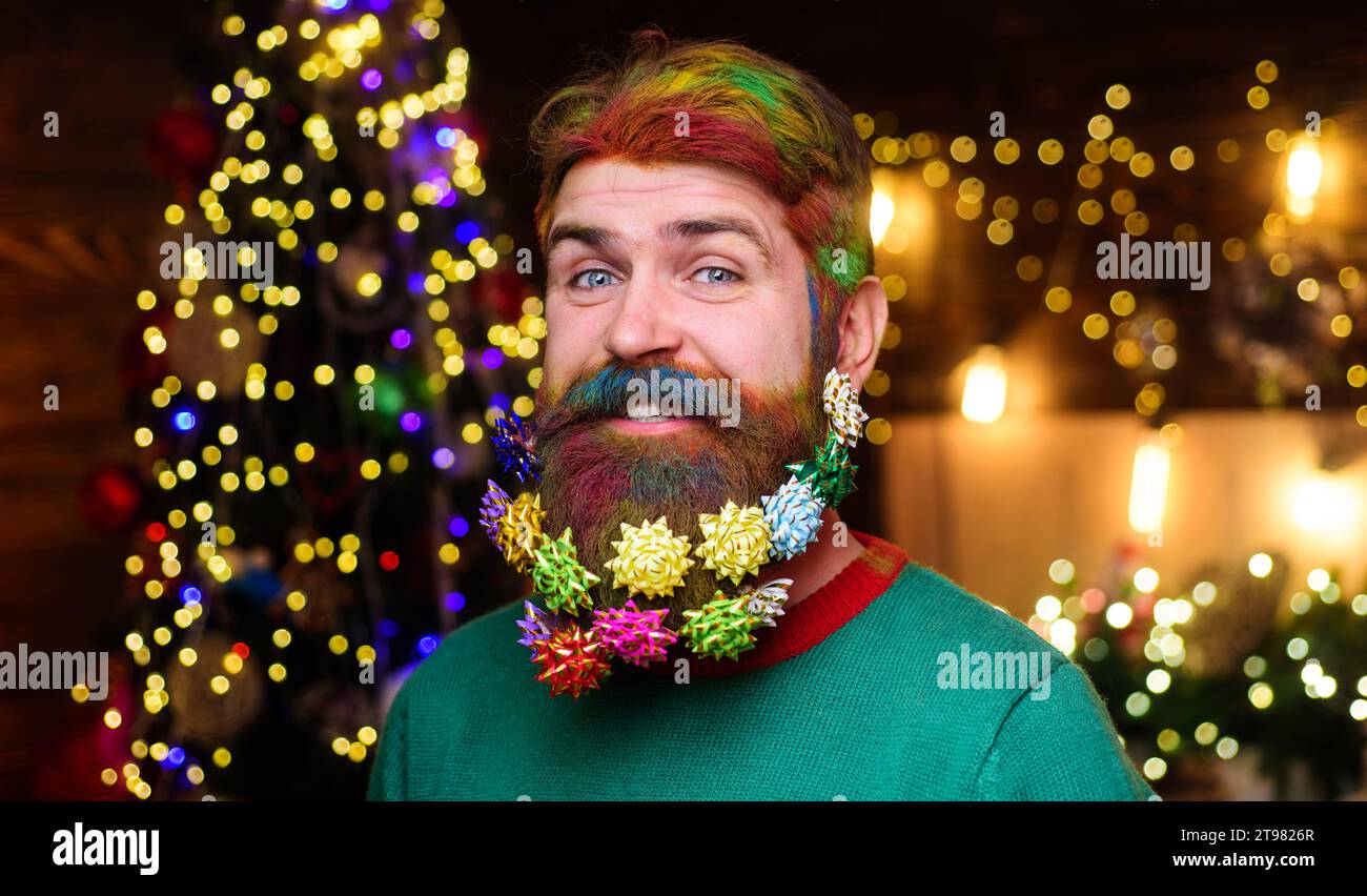 Publicité pour salon de coiffure de Noël. Homme barbu souriant avec des cheveux colorés et barbe avec des décorations de Noël dans la barbe. Hipster barbu avec décoration Banque D'Images