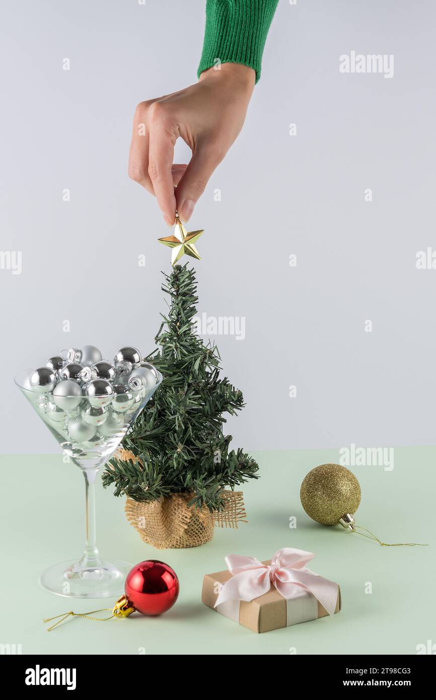 Mise en page créative sur fond vert menthe pastel. Main de femme plaçant la décoration d'étoile de Noël. Fond de fête rétro du nouvel an. Banque D'Images