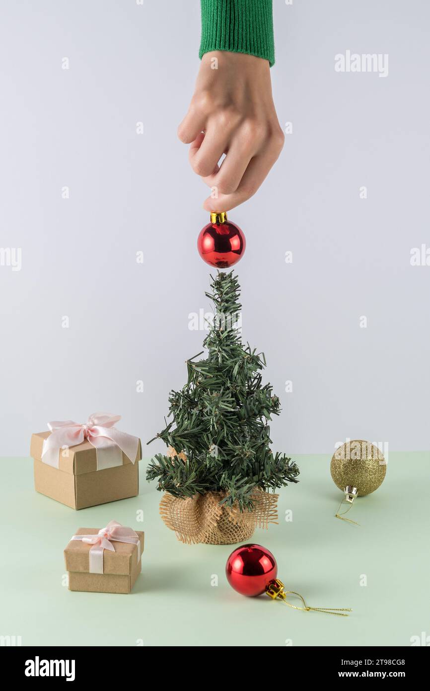 Mise en page créative sur fond vert menthe pastel. Main de femme plaçant la décoration d'arbre de Noël. Fond de fête rétro du nouvel an. Banque D'Images
