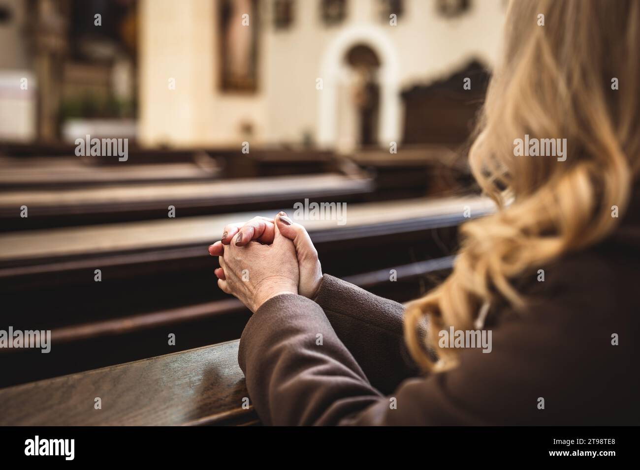 Femme chrétienne avec les mains pliées dans la prière assise sur l'église pew. Religion et spiritualité concept. La personne féminine prie Dieu Banque D'Images