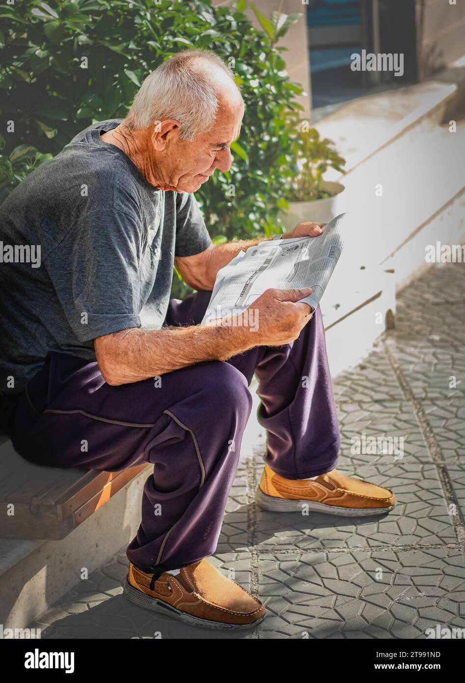 Homme âgé lisant le journal dans la rue. Retraité lisant les journaux dans le parc. Novembre-24,2023 Banque D'Images