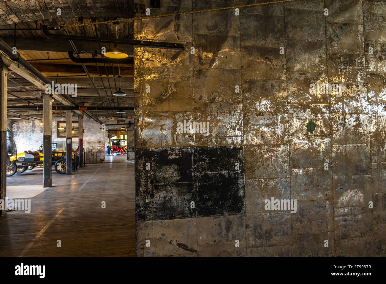 Une porte coulissante en tôle érodée au Ford Piquette Plant à Detroit, Michigan, États-Unis, occupe le premier plan, avec des véhicules historiques alignés sur le sol en bois de la salle de l’usine en arrière-plan. Construit en 1904, le Ford Piquette Plant est considéré comme le plus ancien bâtiment survivant initialement conçu pour la production automobile et encore ouvert au public. Banque D'Images