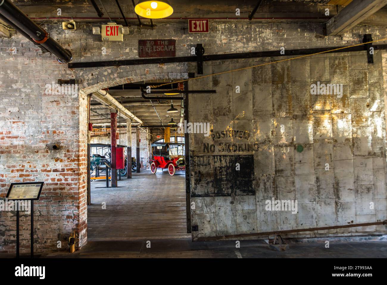 Une porte coulissante lourde revêtue de tôle usée porte encore l'inscription lisible « Positively No Smoking » à l'entrée de l'usine Ford Piquette à Detroit, Michigan, États-Unis. Une Ford Model T rouge historique est visible à travers la porte ouverte. Construite en 1904, l'usine Ford Piquette est considérée comme le plus ancien bâtiment survivant initialement construit spécifiquement pour la production automobile et qui reste ouvert au public. Banque D'Images