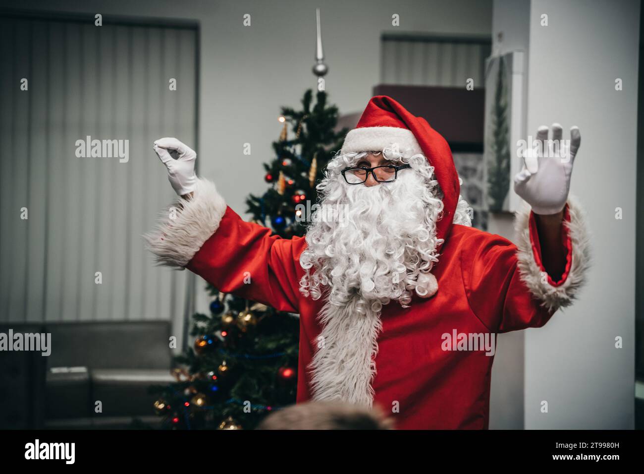 Un Père Noël joyeux avec une barbe blanche et portant un costume rouge avec bordure blanche, agitant les deux mains dans un geste amical Banque D'Images