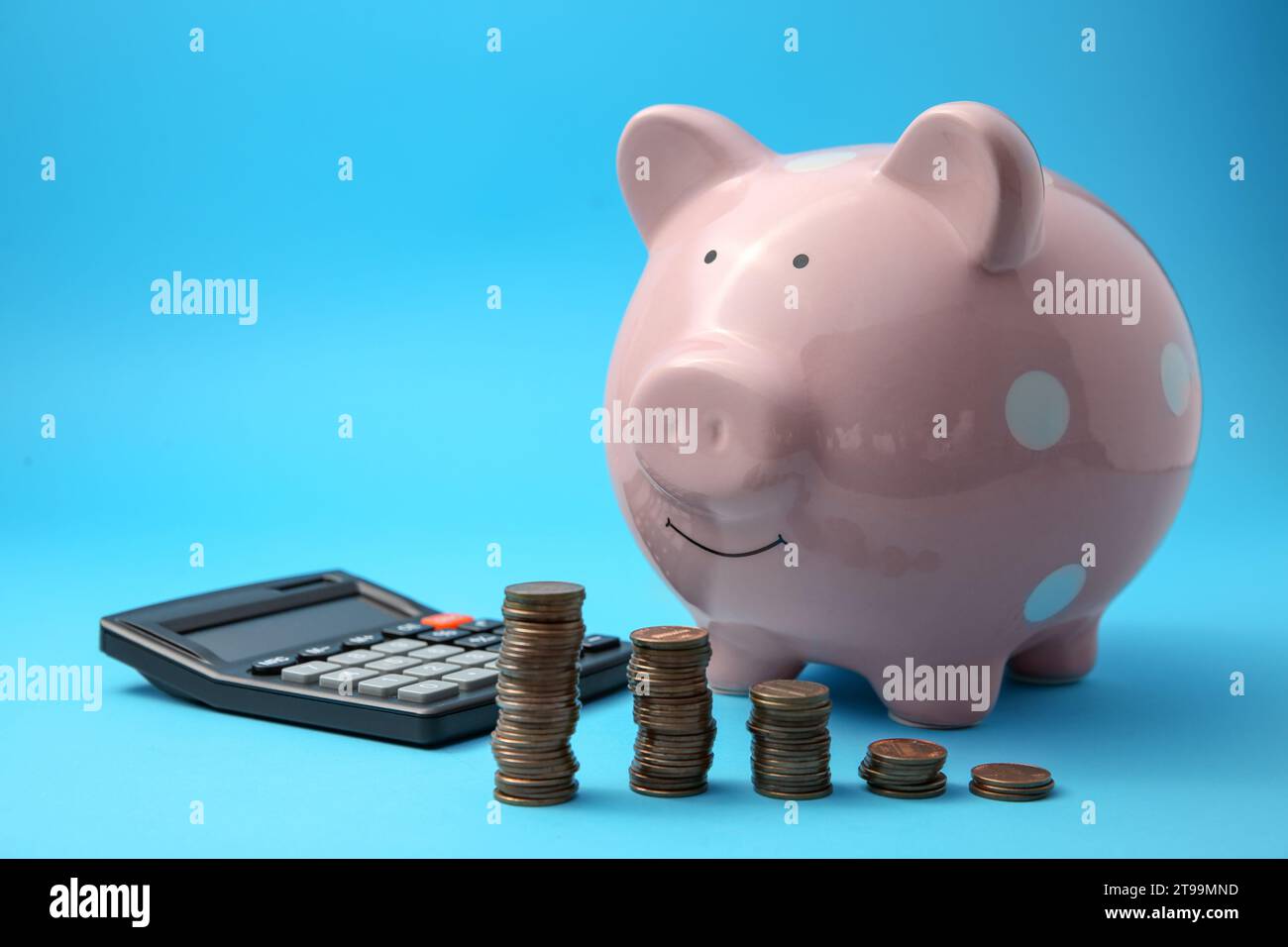 Tirelire, piles de pièces et calculatrice sur fond bleu clair Banque D'Images