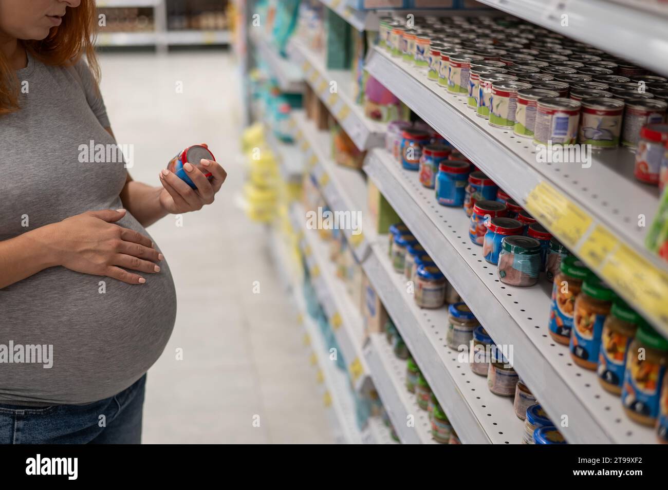 La femme enceinte caucasienne choisit la nourriture pour bébé dans le magasin. Pots avec purée de légumes. Banque D'Images