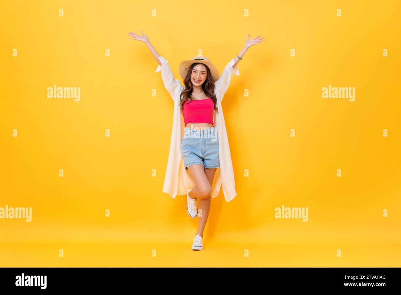 Portrait de corps entier de jolie femme asiatique portant la tenue d'été souriant et levant les mains vers le haut dans fond jaune coloré isolé studio shot Banque D'Images