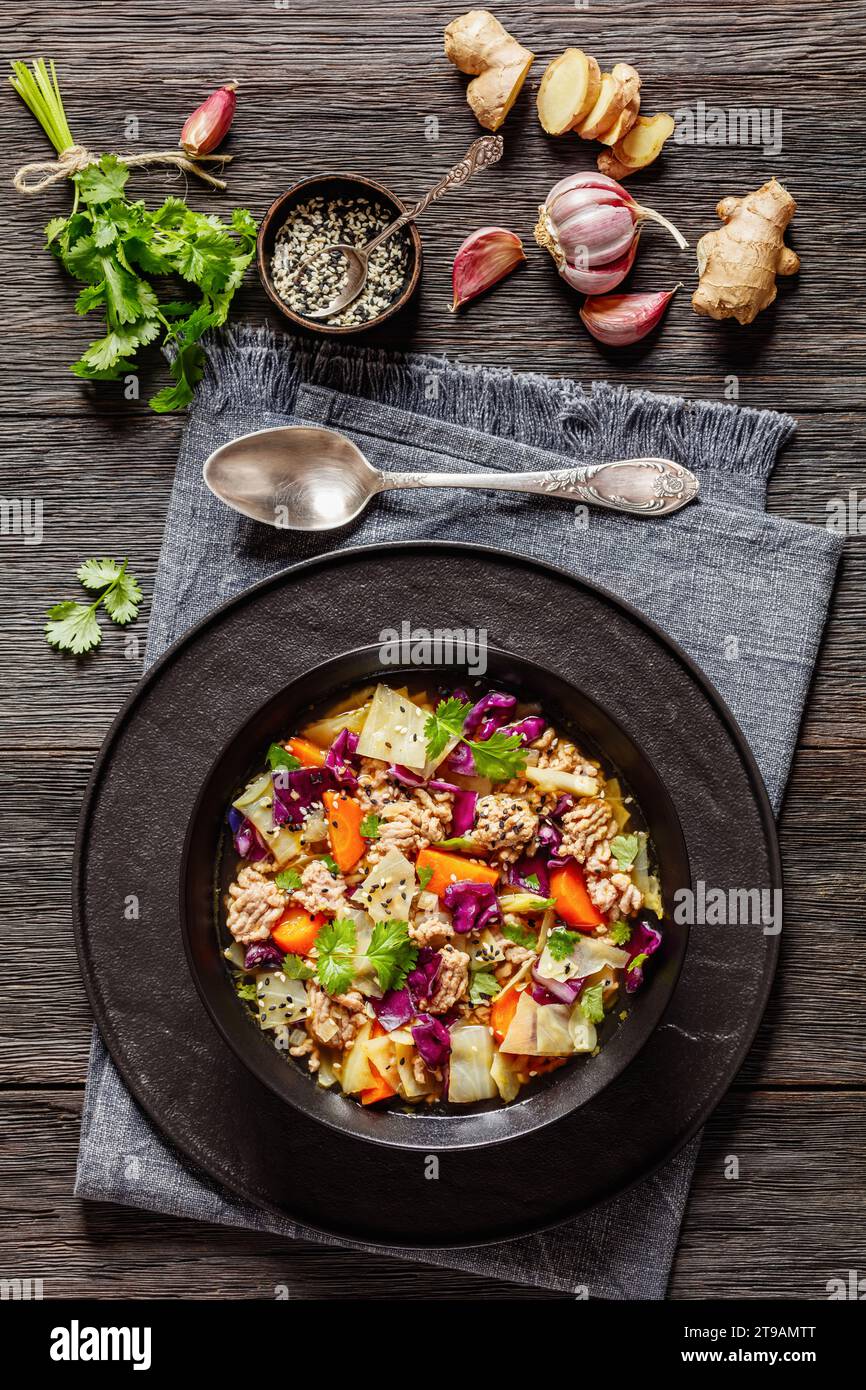 soupe au chou roulé aux œufs avec du porc haché et des légumes dans un bol noir sur une table en bois sombre avec des ingrédients, cuisine asiatique, vue verticale d'en haut Banque D'Images