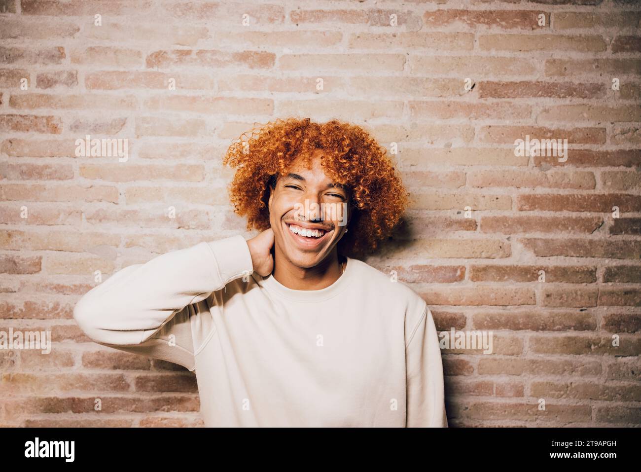 Portrait d'un jeune homme afro-américain souriant avec coiffure afro avec un fond de mur de briques. Banque D'Images