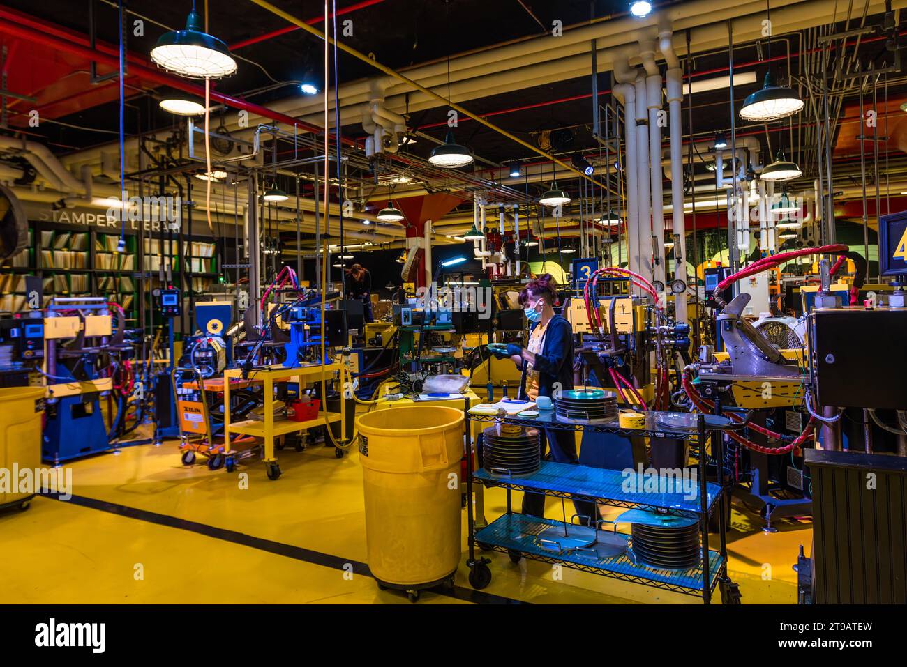 Un employé masqué actionne les cadrans et les écrans d'une machine de pressage à Third Man Pressing à Detroit, Michigan, États-Unis, avec des disques empilés à portée de main sur un chariot roulant bleu. L'usine de pressage du label vinyle indépendant Third Man Records (fondé par Jack White, Ben Blackwell et Ben Swank) fonctionne dans la rue Canfield du Cass Corridor depuis 2017. Banque D'Images