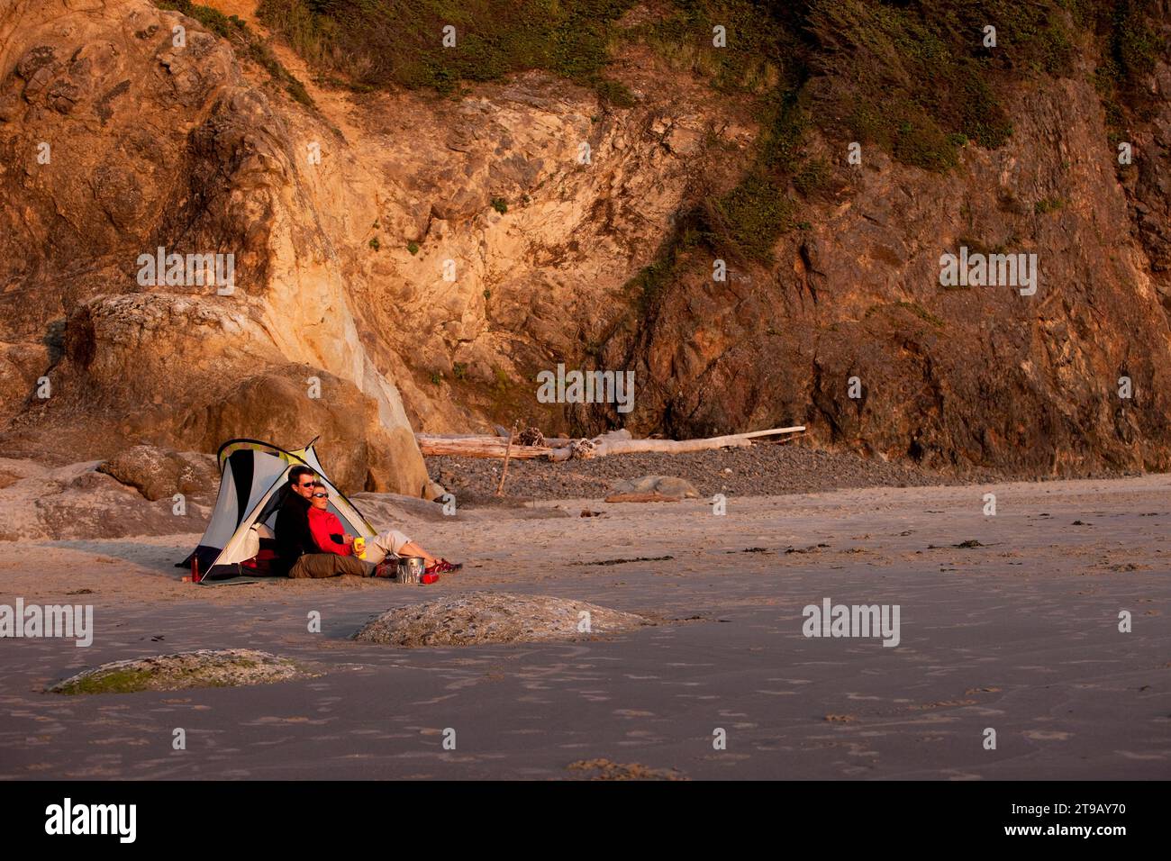 Couple mâle et femelle profitant l'un de l'autre et le coucher du soleil tout en campant sur la plage. Banque D'Images