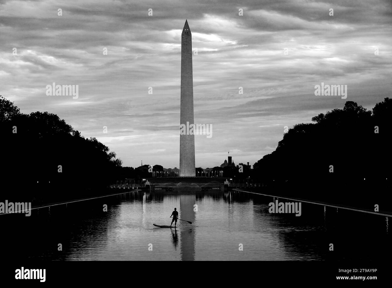 Image en noir et blanc d'un homme debout paddleboard (SUP) dans une piscine réfléchissante et regardant vers le haut un mémorial national. Banque D'Images