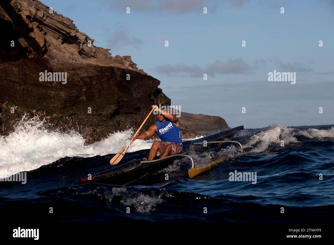 Un homme pagayant un canot en saillie à côté de grandes falaises et de vagues qui se brisent. Banque D'Images