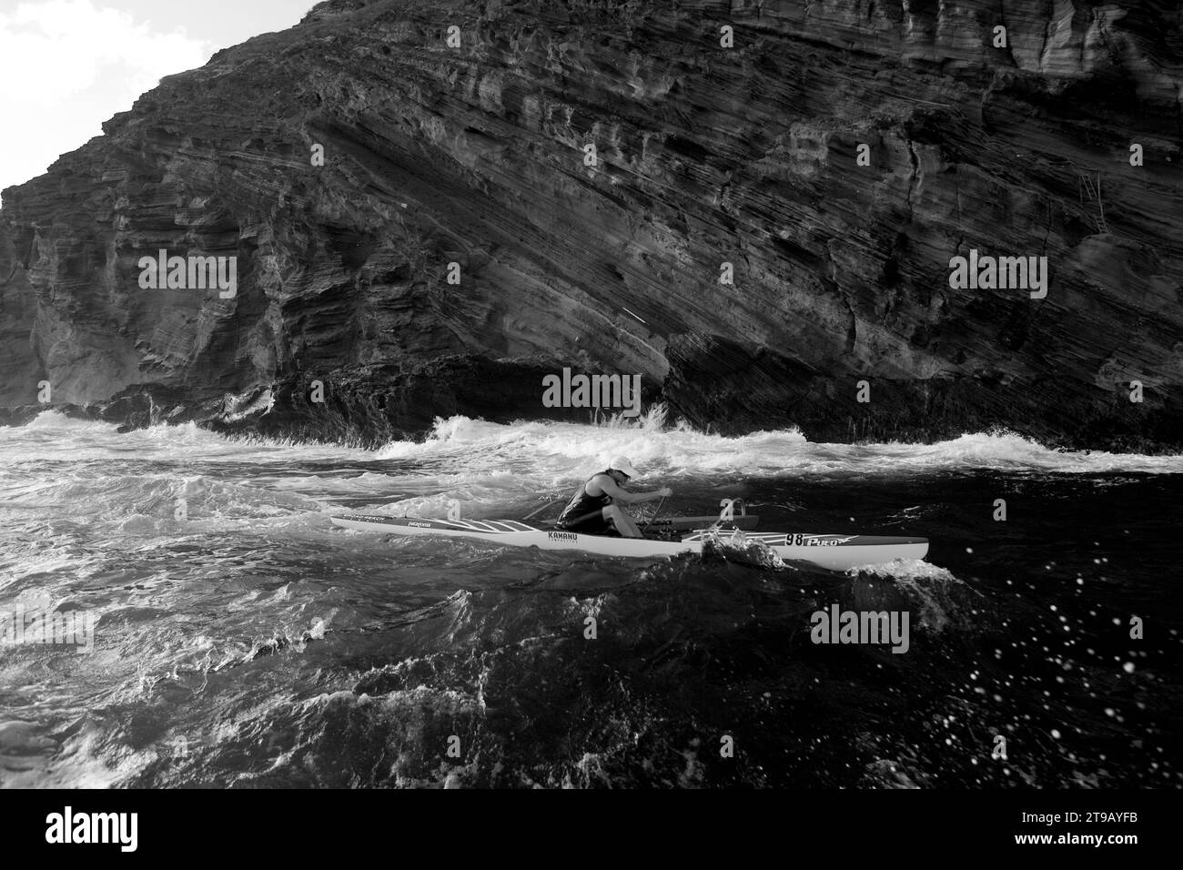 Image en noir et blanc d'un homme pagayant un canot en saillie à côté de grandes falaises. Banque D'Images