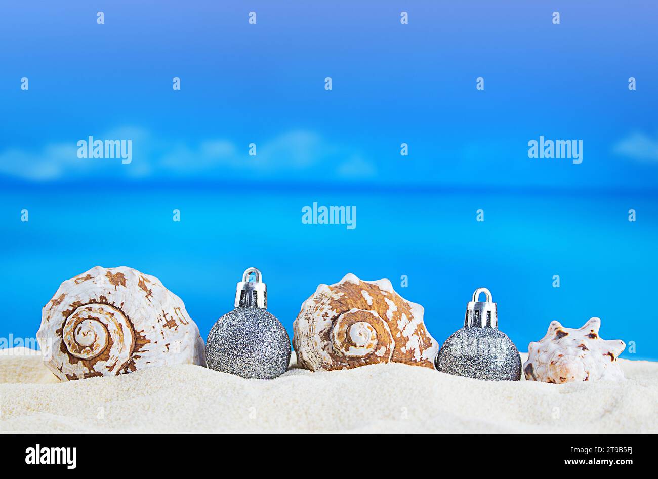 Coquillages blancs avec des boules brillantes argentées d'arbre de Noël sur le sable de la plage sur la journée ensoleillée avec la mer. Nouvel an, vacances dans les pays chauds. Copier sp Banque D'Images