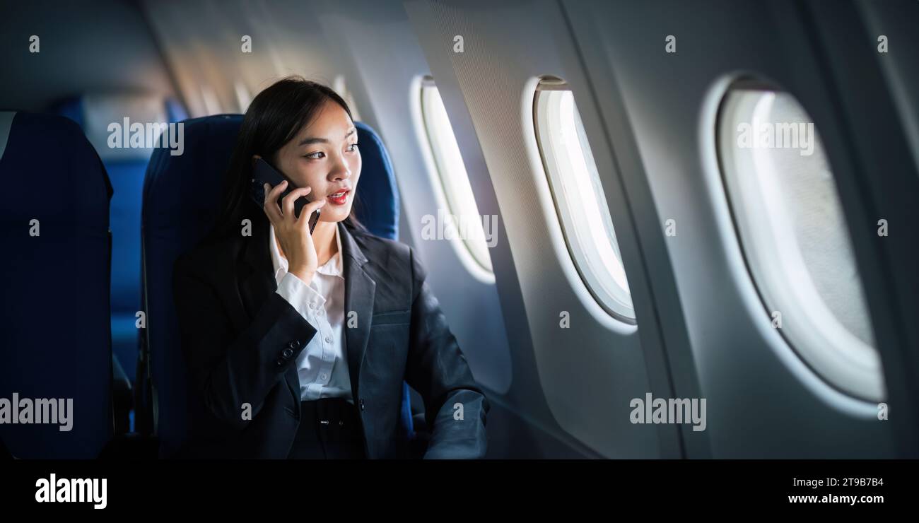 Femme d'affaires asiatique réussie, femme d'affaires travaillant dans l'avion sur ordinateur portable et regardant par la fenêtre avec parler au téléphone Banque D'Images