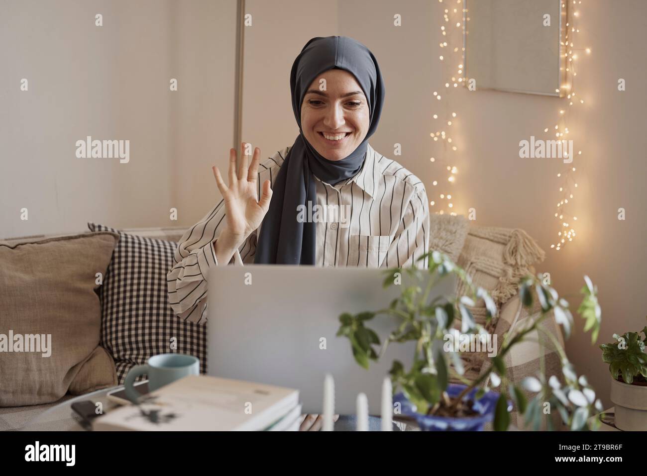 Heureuse femme freelance agitant sur appel vidéo sur ordinateur portable tout en travaillant à la maison Banque D'Images
