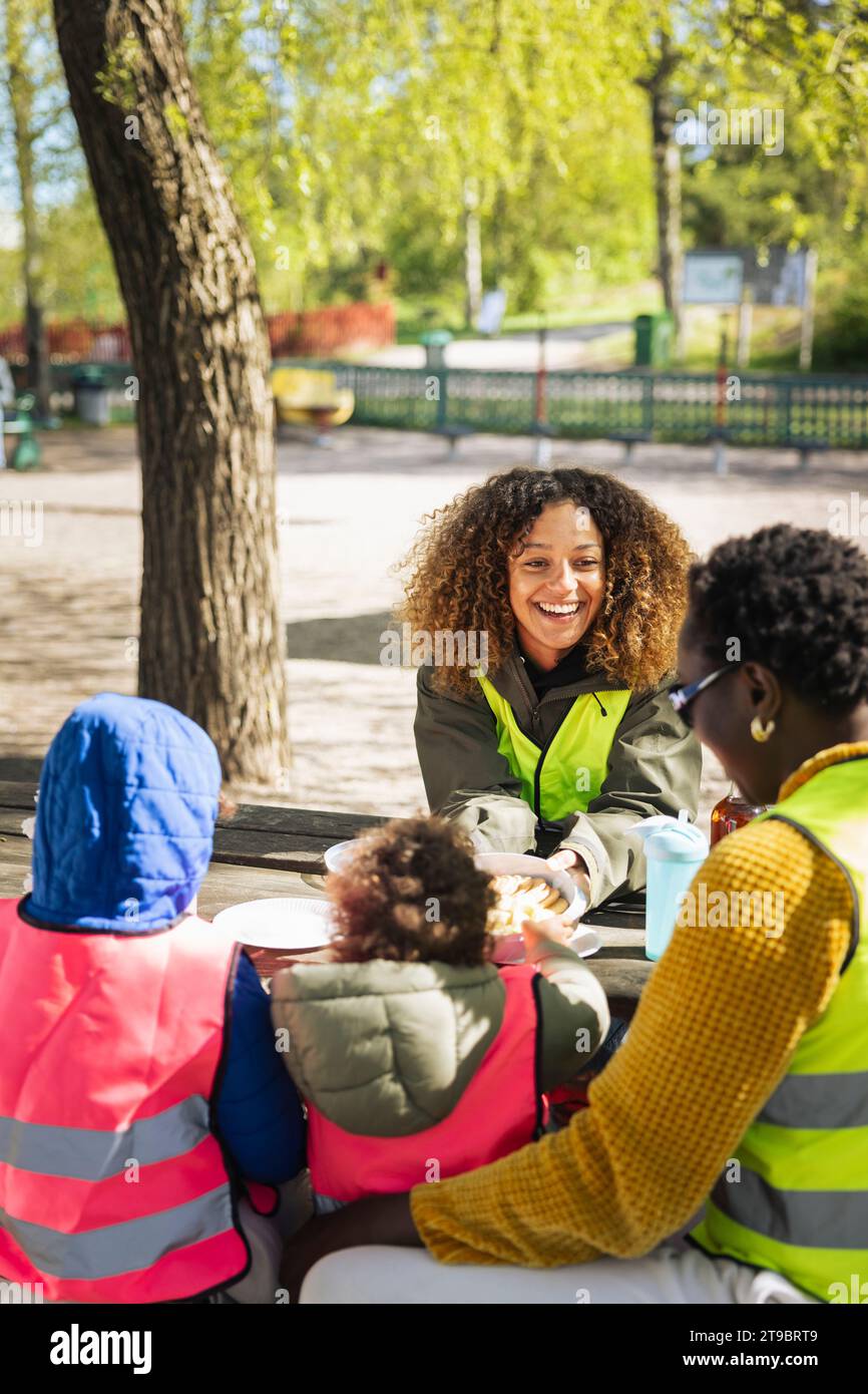 Femme souriante parlant avec une amie assise par les enfants à table Banque D'Images