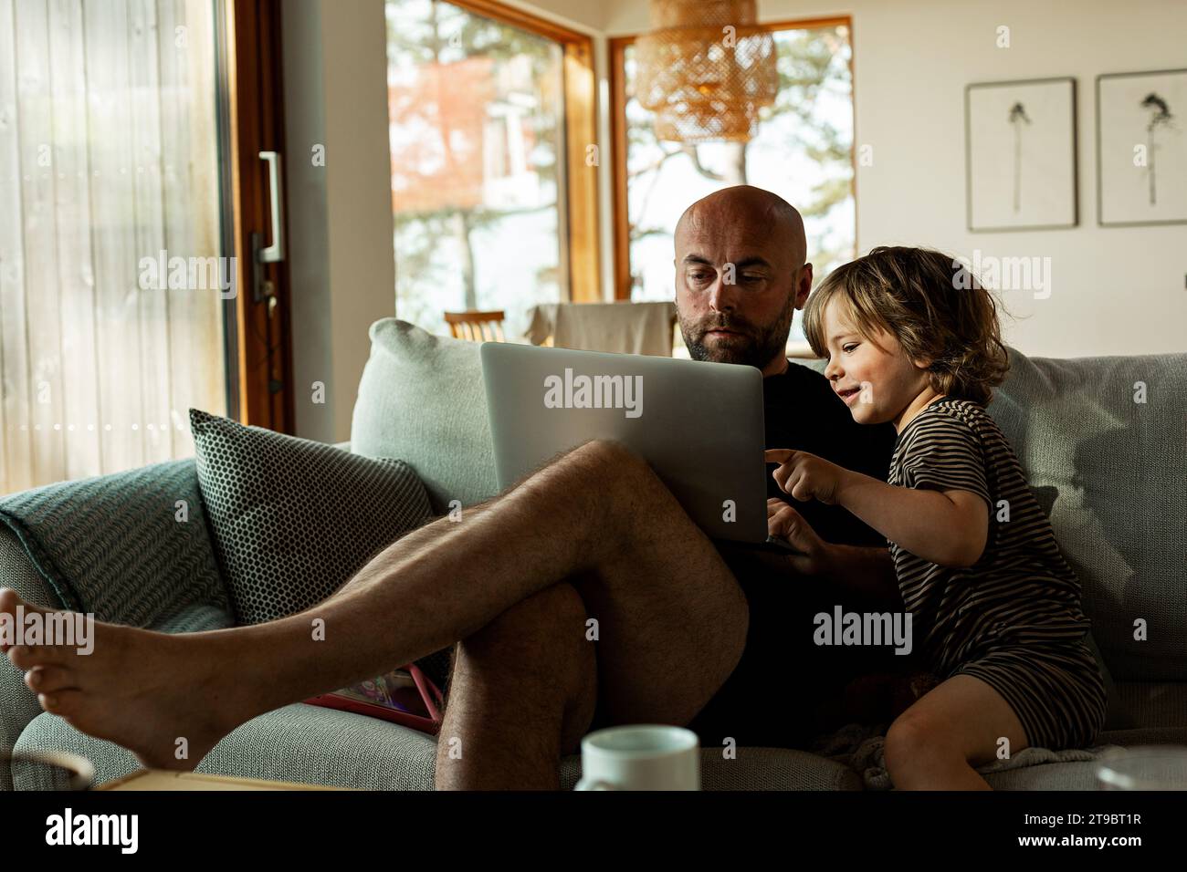 Homme freelance utilisant ordinateur portable et fils regardant tout en étant assis sur le canapé dans le salon Banque D'Images