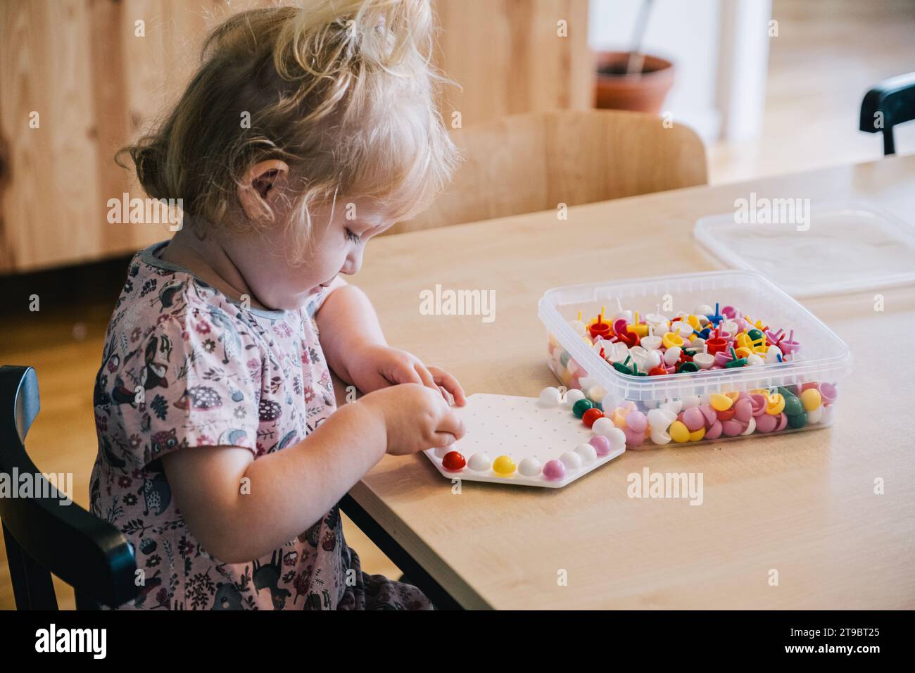 Fille blonde jouant avec le jeu de pegboard sur la table à la maison Banque D'Images