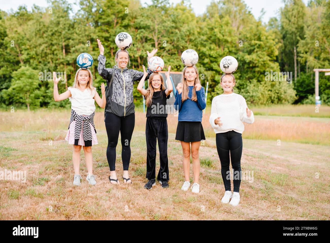 Femme heureuse avec des filles équilibrant des ballons de football sur la tête tout en se tenant debout sur l'herbe Banque D'Images