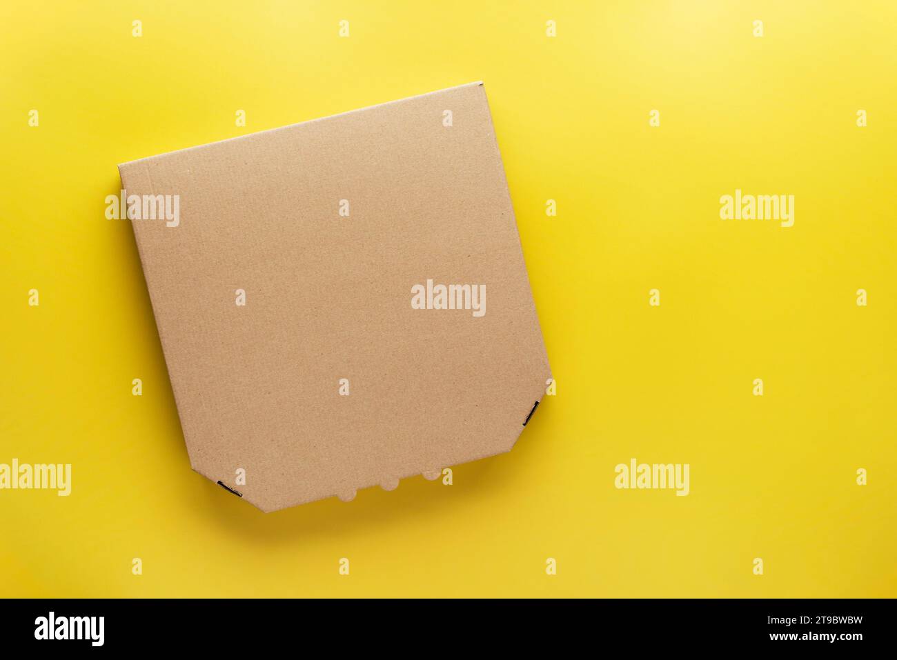 Boîte de carton fermée de pizza sur fond jaune uniforme maquette de pose plate avec espace vide Banque D'Images