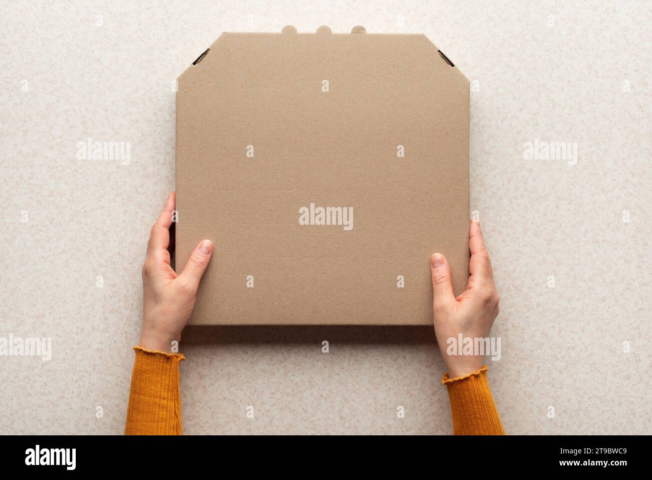 Boîte de carton fermée de pizza dans les mains caucasiennes sur la table de cuisine plate maquette de pose avec l'espace de copie Banque D'Images
