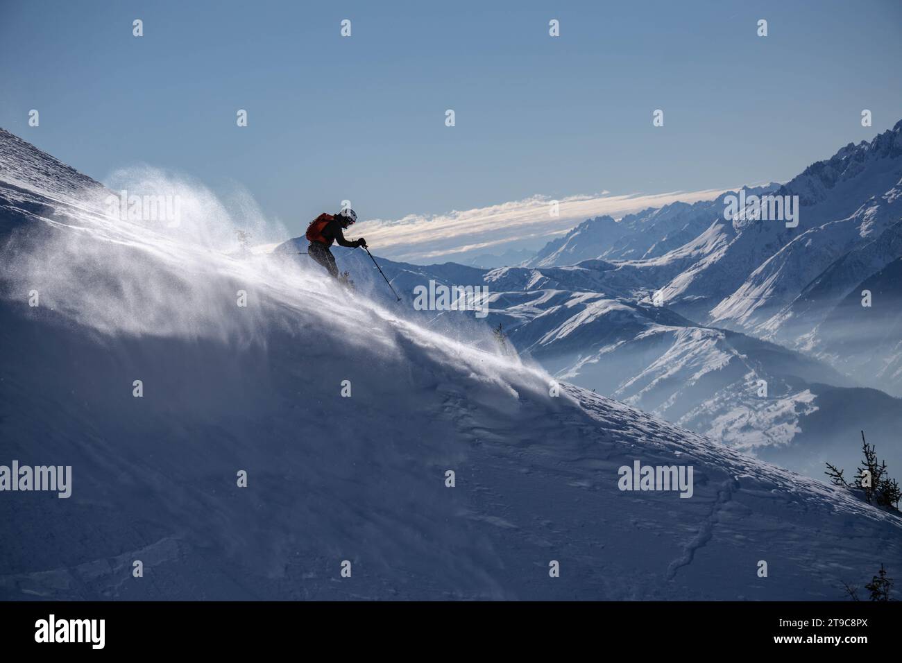 Garçon skiant dans les montagnes, créant une vague de neige blanche comme il descend.montagnes et un ciel bleu en arrière-plan. France, Alpes franches. Banque D'Images