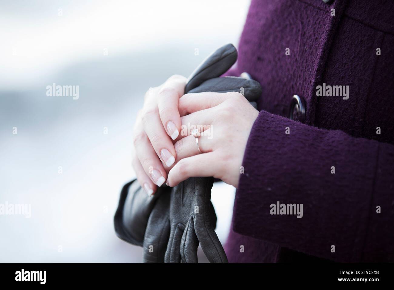 Gros plan de femmes blanches caucasiennes mains manucurées tenant des gants en cuir noir, contre un manteau de laine d'hiver violet Banque D'Images