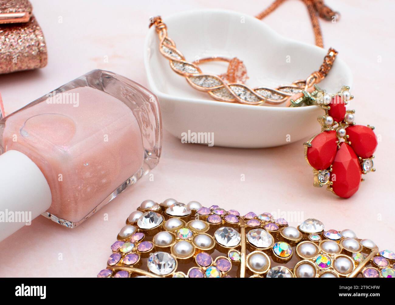 Concept de mode et de bijoux plat en or rose avec fond de quartz rose, vernis à ongles rose, pochette à paillettes et bijoux en diamant en or rose Banque D'Images