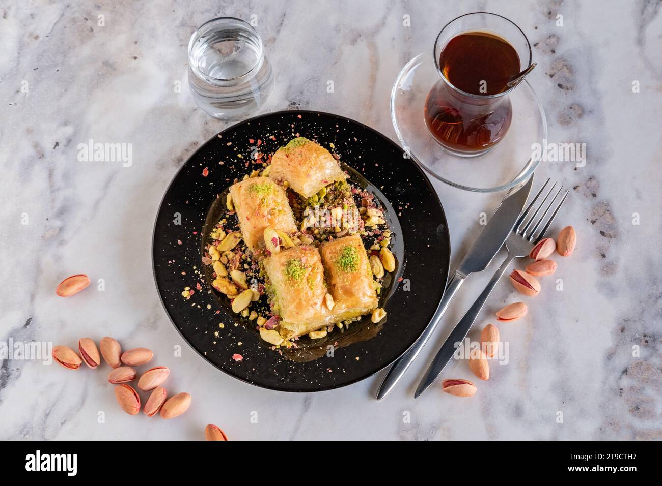 Baklava traditionnel turc célèbre dessert, pistaches et verre à thé dans une assiette noire sur fond de marbre Banque D'Images