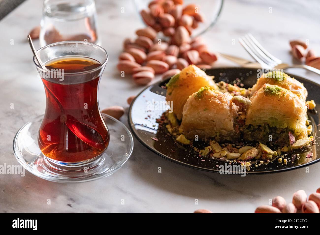 Baklava traditionnel turc célèbre dessert, pistaches et verre à thé dans une assiette noire sur fond de marbre Banque D'Images