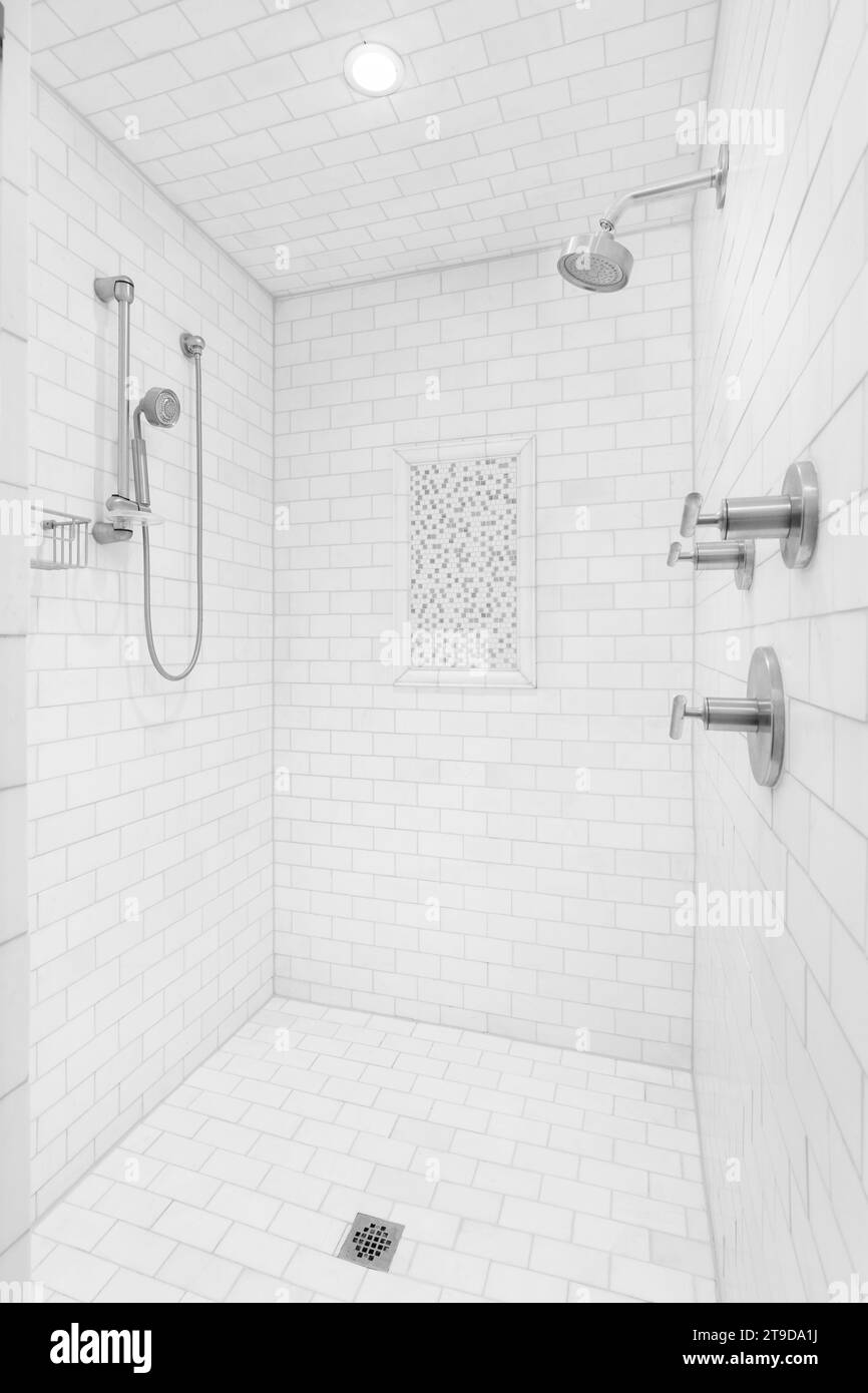Une grande douche de plain-pied avec carreaux de métro sur les murs et le sol, pommes de douche chromées et robinet, et un petit accent de carreaux carrés. Banque D'Images