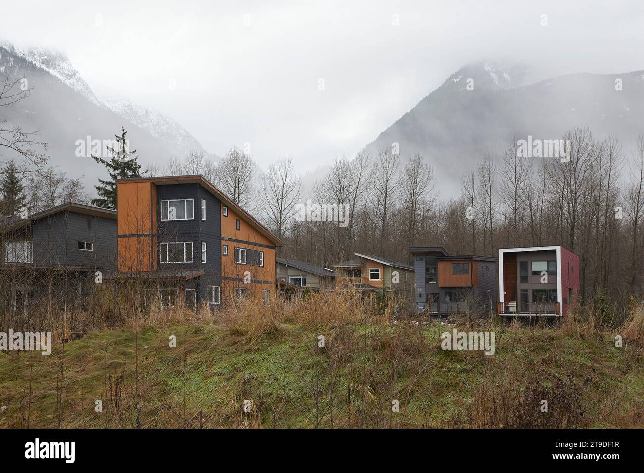 Chalets unifamiliaux, maisons construites sur la digue à côté de la rivière Squamish, montagnes côtières enneigées derrière. Banque D'Images