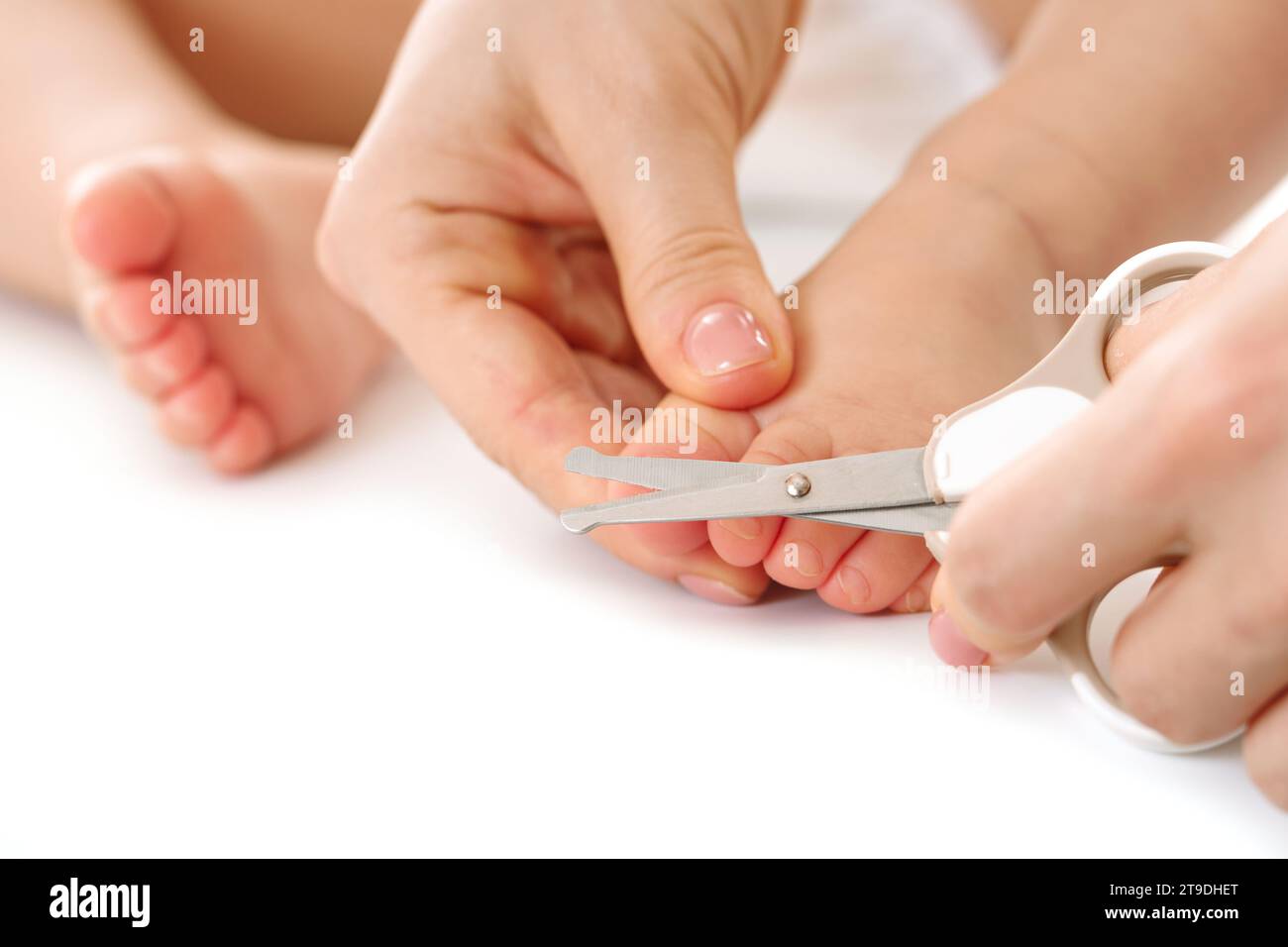 Plan rapproché d'une mère tenant doucement le pied de son petit enfant et coupant les ongles de pied sur fond blanc. Banque D'Images