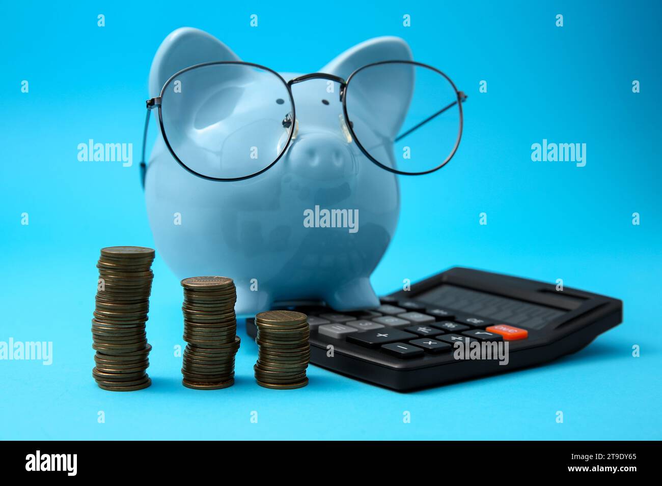 Tirelire dans des verres, des piles de pièces de monnaie et calculatrice sur fond bleu clair Banque D'Images