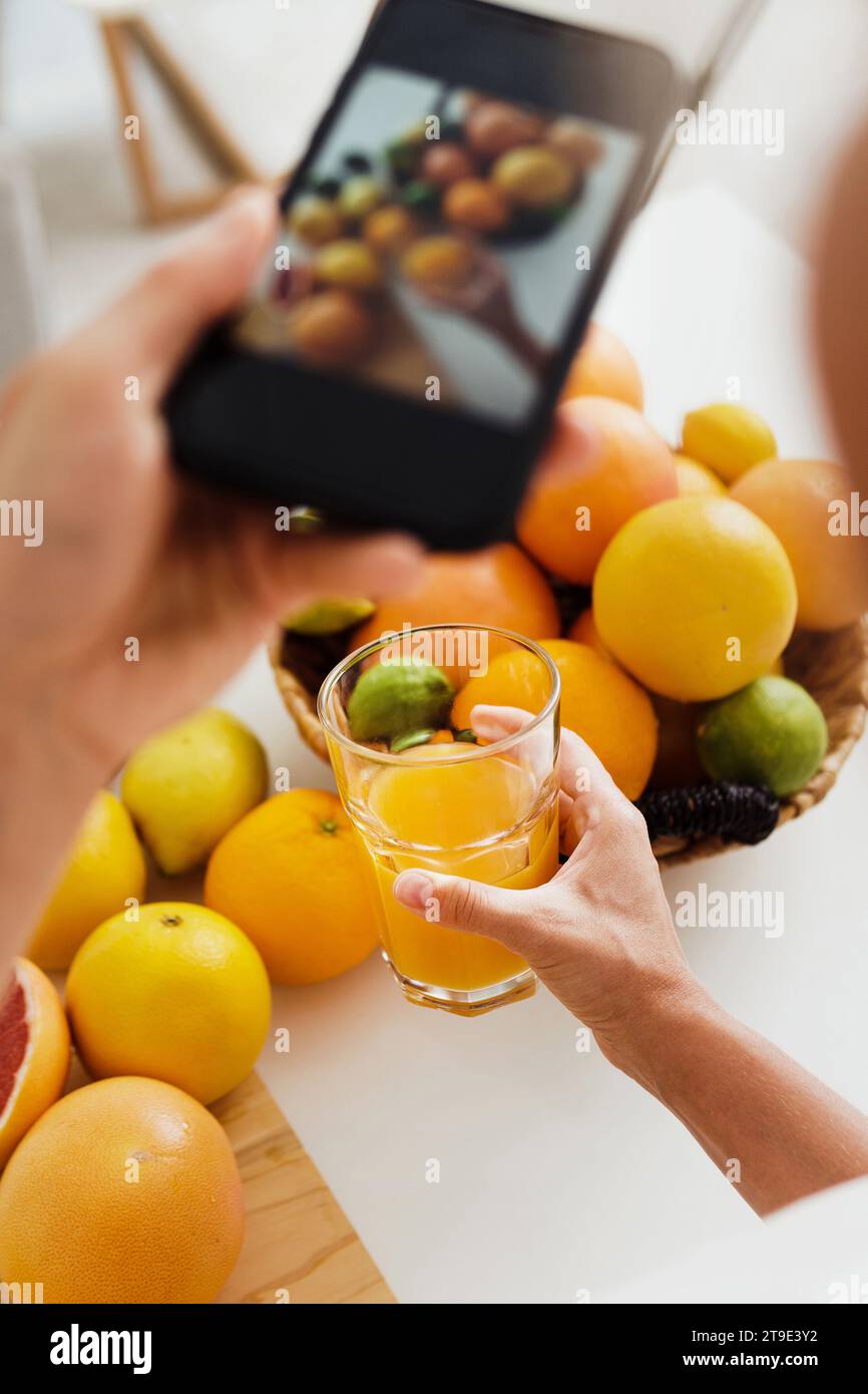 Gros plan de la main féminine avec un smartphone prenant des photos de verre avec du jus d'orange Banque D'Images