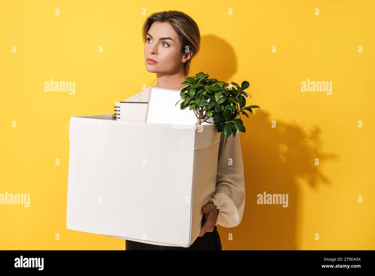 Jeune femme tenant la boîte avec des objets personnels après la démission de l'emploi sur fond jaune Banque D'Images
