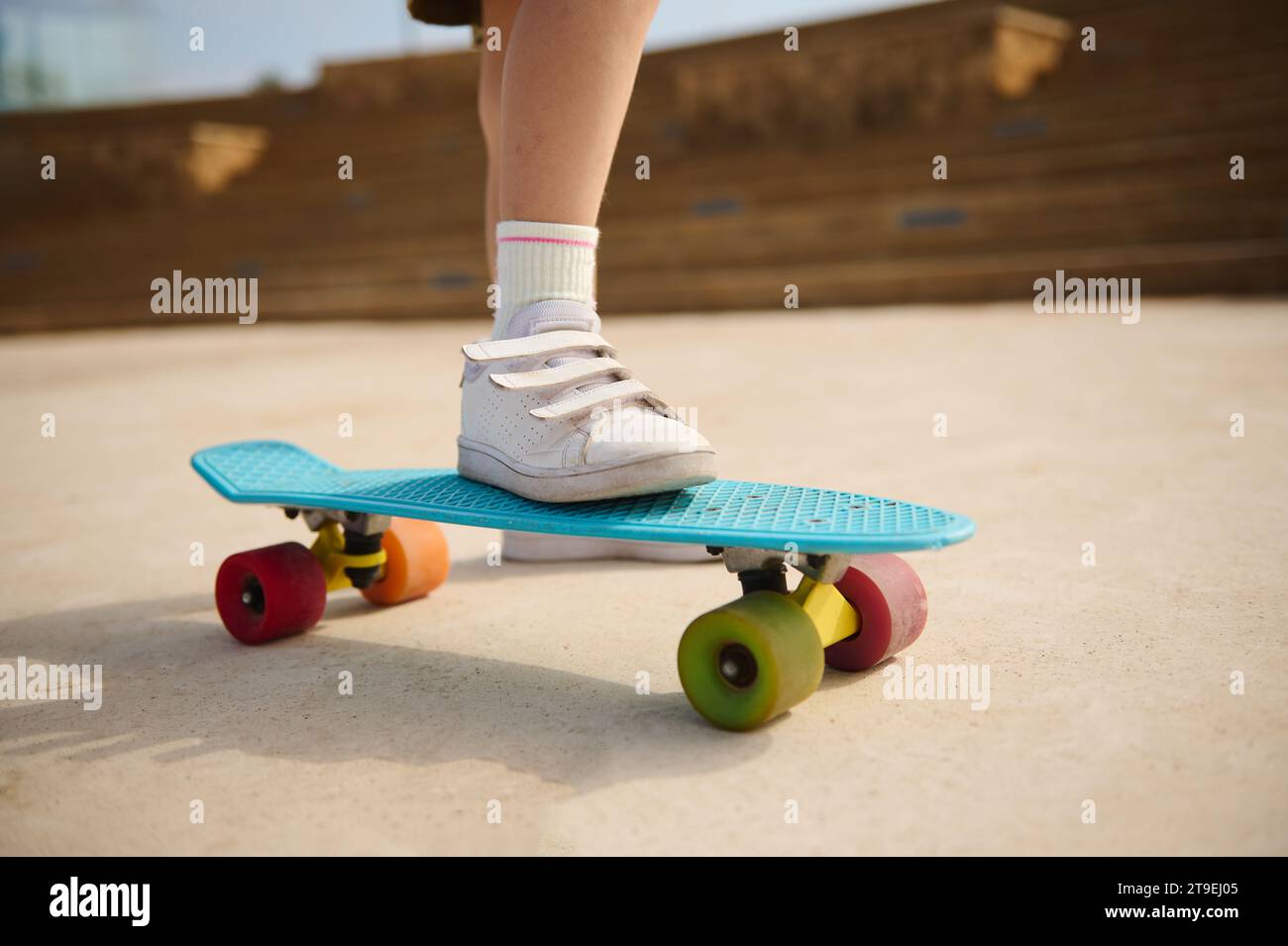 Gros plan roues de skate multicolores et pied ou jambe sur le dos de l'enfant ou de la petite fille jouant à la planche à roulettes, ou le patin de surf et commencer sur la piste de pompe en plein air à sk Banque D'Images