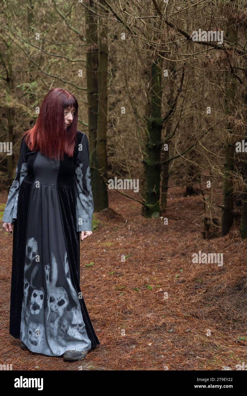 femme en robe noire et grise avec manches chauve-souris et crânes se tenait dans une forêt Banque D'Images