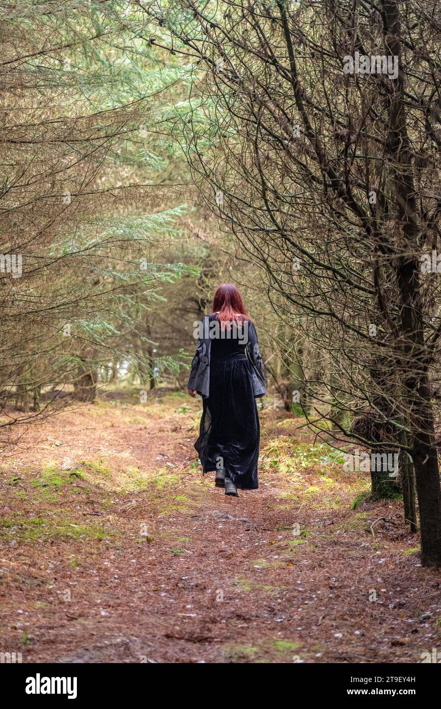femme en robe noire et grise avec manches de chauve-souris et crânes marchant loin de la caméra dans une forêt Banque D'Images