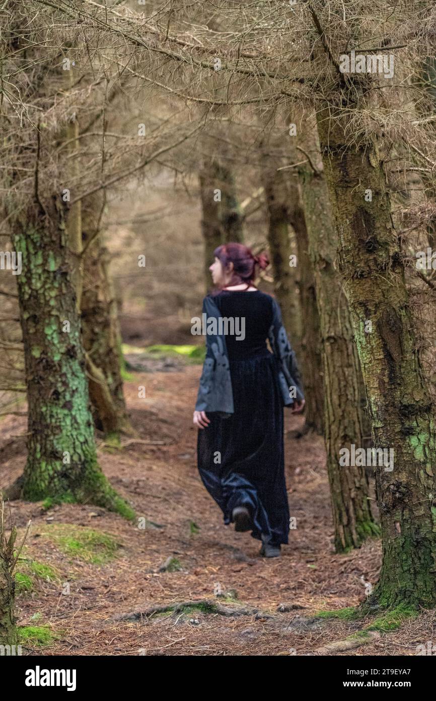 femme en robe noire et grise avec manches de chauve-souris et crânes marchant loin de la caméra dans une forêt Banque D'Images