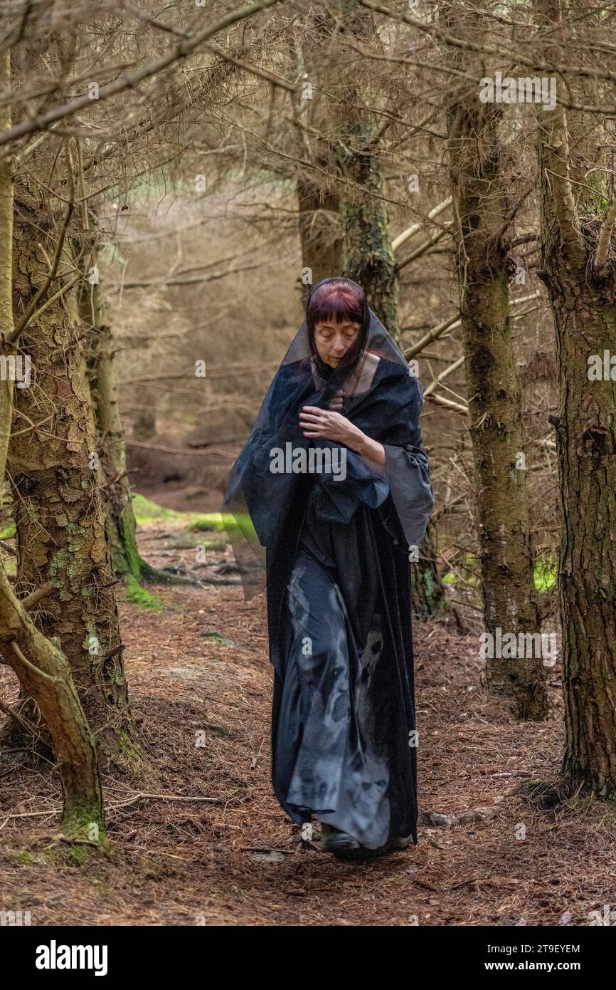 femme en robe noire et grise avec manches chauve-souris et crânes se tenait dans une forêt Banque D'Images