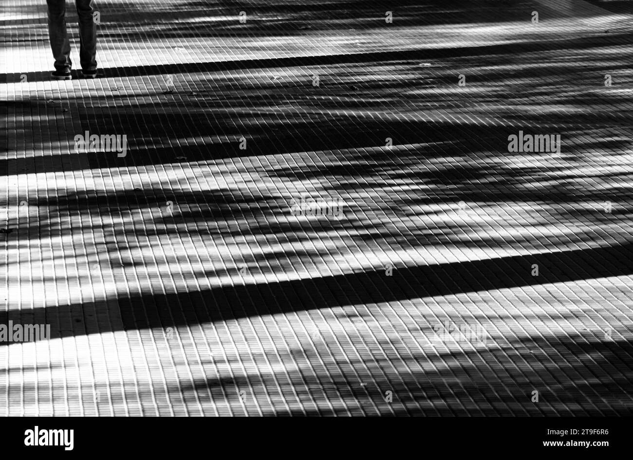 Ombres sur une passerelle piétonne pavée de la ville avec des jambes d'une personne en noir et blanc contraste élevé Banque D'Images