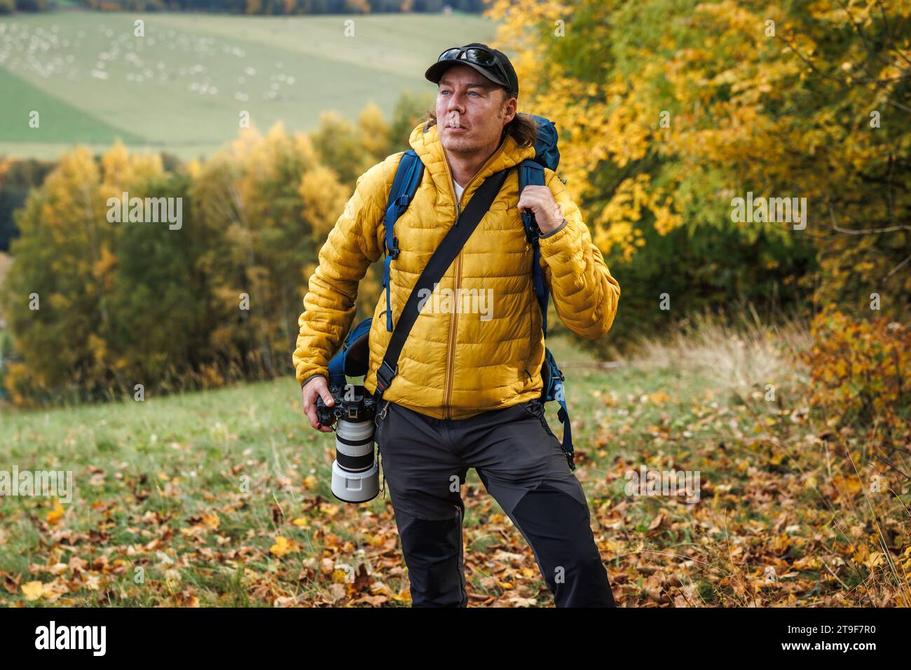 Photographe animalier explorant la forêt et l'observation des oiseaux. Homme avec veste jaune et caméra randonnée dans les bois d'automne Banque D'Images