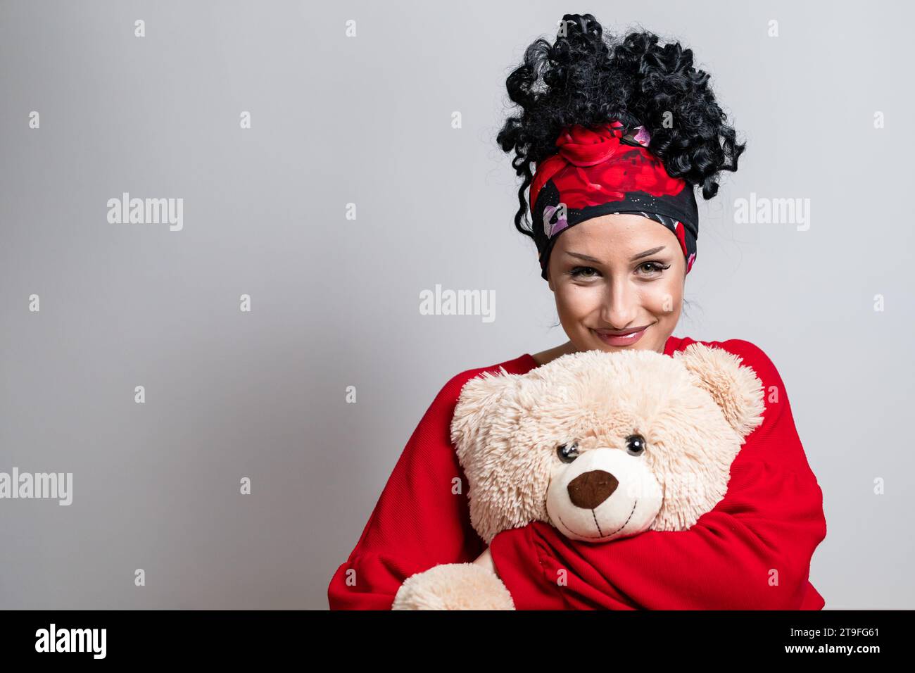 Belle jeune fille bouclé avec coiffure bandana tenant un ours en peluche Banque D'Images