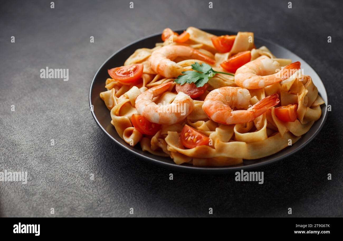 Pâtes fettuccine avec crevettes et tomates sur plaque grise, sur fond sombre, mise au point sélective, effet bokeh. Banque D'Images