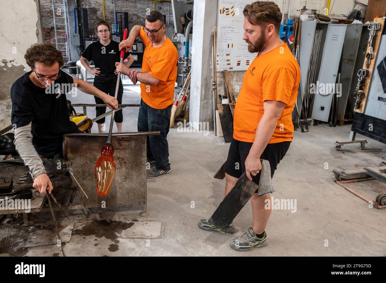 Un souffleur de verre façonne habilement un moule en fusion chauffé de verre clair en un vase à fleurs fabriqué à la main avec l'aide de certains de ses collègues du W Banque D'Images