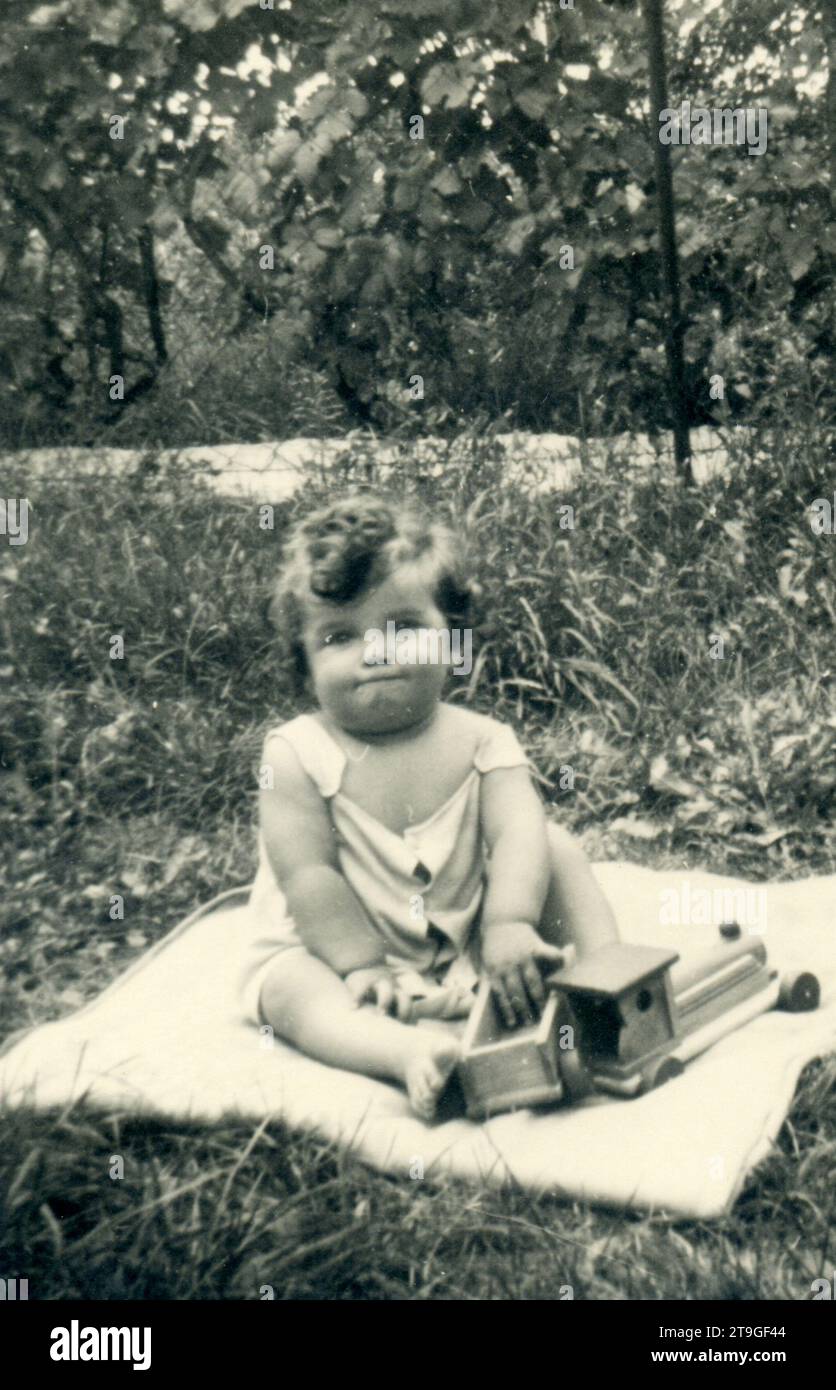 le tout-petit fille des années 1940 joue avec le train en bois jouet sur la pelouse Banque D'Images